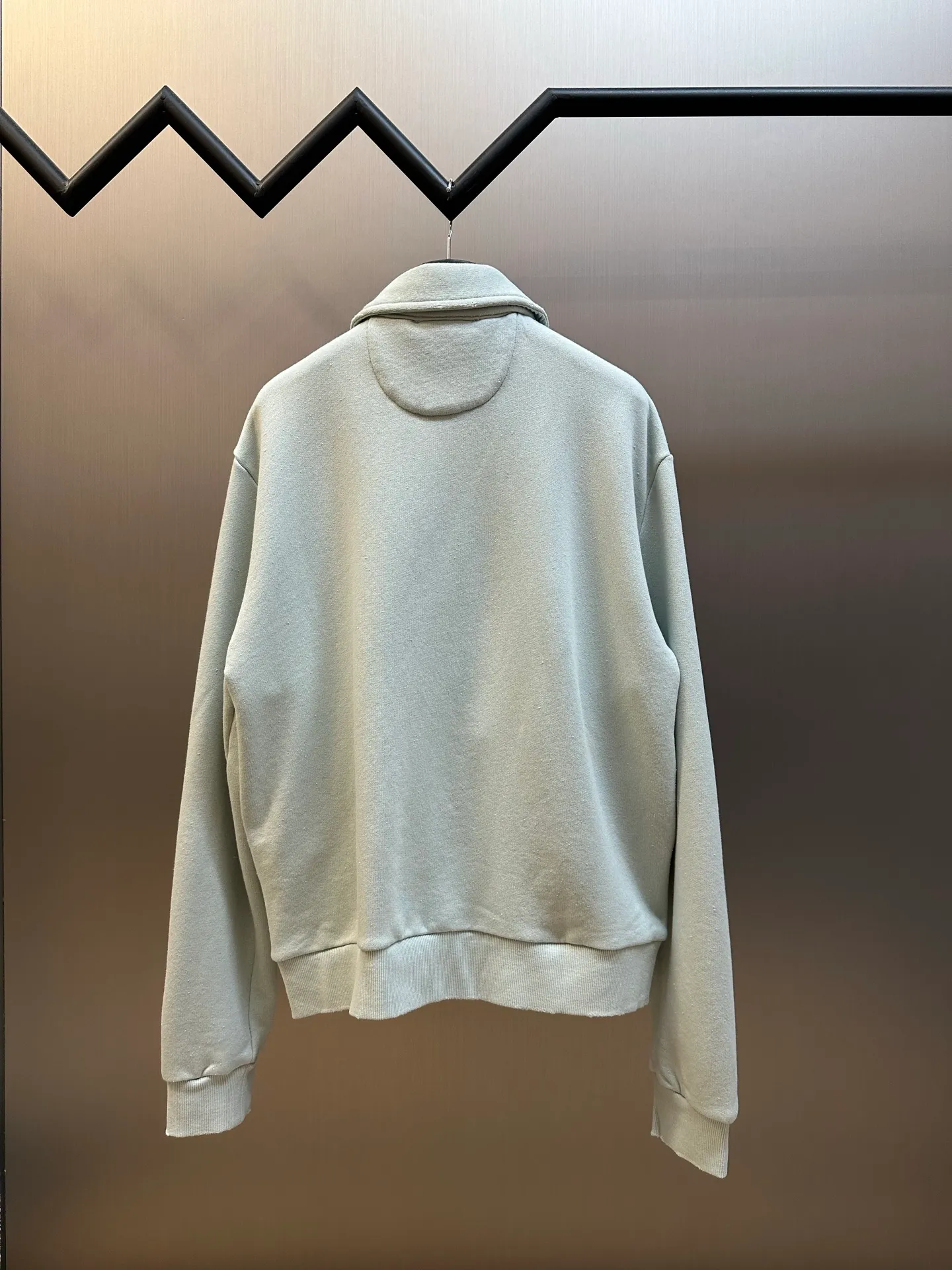 Ac vintage collared zipper sweatshirt uses 32-count top layer and 40-count bottom layer of 3-strand composite fleece structure, with a weight of g/㎡. The 32-count yarn on the top layer is fine and smooth, giving the surface a smooth touch and excellent anti-pilling properties; the 40-count 3-ply yarn on the bottom layer is treated with a raising process to form a rich and soft fluff layer, providing excellent warmth and skin-friendly wrapping. With 21 2×2 ribs, the g/㎡ weight ensures that the collar, cuffs and hem have excellent tensile fatigue resistance and shape retention capabilities. During piece dyeing, the entire fabric is immersed in the dye vat after weaving, and the dye molecules fully penetrate into the fibers, ensuring full, deep colors and excellent color fastness. Each batch of dyeing produces subtle differences, making the color tone of the single product unique. On this basis, the paint is sprayed irregularly on the surface of the garment through manual spray painting to create a splash-like retro effect. The distressed processing of holes causes the color to fade and mottle in parts. The ribbed trim is also treated to form slight whitening and fluffing, which visually echoes the spray-painted effect on the body, making the new clothes appear as if they have been worn for a long time and exposed to the sun. The front logo stamp uses a slurry printing process. The printing slurry contains a special microcapsule foaming agent. After being baked at high temperature, the slurry layer expands to form three-dimensional bulges, and the surface presents a granular texture similar to inkjet paint. This process simulates the effect of random drops of pigment after being atomized during spray gun spraying. The edges of the pattern present a natural feathering transition, rather than the rigid boundaries of glue printing. The printing surface has a fine graininess and soft elasticity to the touch, forming a closed loop of the process with the distressed effect of the spray painting on the body. size：xs s m l